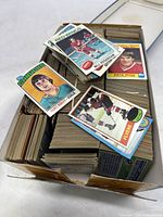 Photo showing shoebox with many stacks of vintage hockey and sports cards, with several card faces visible on top including Curt Ridley and Bill Hogaboam.