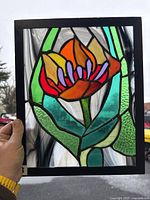 Front view of stained glass art panel held by hand showing vibrant flower design against swirled clear glass background.