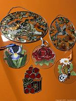 All 6 sun catchers grouped on orange surface showing designs of birds, flowers, butterfly and strawberries.