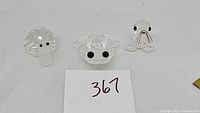 Front view of three Swarovski crystal figurines: snail, frog, walrus, arranged on plain background.