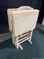 Four folding wooden tray tables stacked in a stand with smooth light wood finish and rectangular tops with rounded corners.