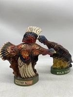 Two vintage Wild Turkey ceramic decanters shaped like turkeys, one larger and one smaller, standing on green bases with brand markings.