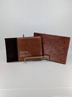 Three 1976 Olympic stamp souvenir books in brown and rust felt with minor exterior blemishes and embossed Olympic rings on cover.