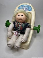 Full view of the 1983 Cabbage Patch Kids doll seated in the plastic carrier with belt accessory visible