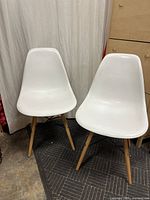 Two white chairs with molded plastic seats and wooden legs shown side by side