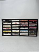 Front view of black cassette tape rack filled with 40 cassette tapes showing artist and album titles.