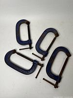 Four blue cast iron Record C-clamps arranged on a white surface showing all clamps together with visible rust and wear.