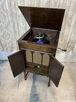 Overall front view of the antique phonograph cabinet with lid open and doors open, showing the turntable and tonearm inside