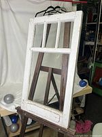 Front-right angled view of antique storm window showing white wooden frame, multiple glass panes, and the condition of the paint and wood.