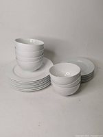 Stack of 8 large plates, 7 bowls stacked on top, and 6 side plates stacked separately all in white porcelain