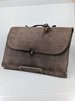 Front view of the brown soft leather laptop bag, flap closed with a small leather strap and button.