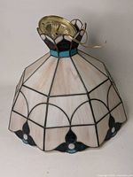 Full view of stained glass ceiling light shade showing pink paneled glass with black and turquoise accent design and wired brass mounting base.