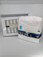 Two twin bed sheet sets displayed: Essential 250 thread count set in zippered packaging and white Easy Care 3-piece sheet set in plastic wrapper.