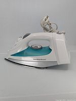 Side and top angled view showing iron body, temperature dial, and cord wrapped loosely around winder at bottom.