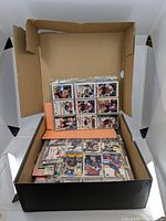 Box filled with hockey cards, some sleeved, some loose, showing multiple players in colorful jerseys from the 1990s era.