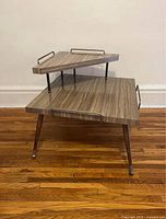 Side view of vintage 2-tiered coffee table showing wood-grain surfaces, metal railings, and angled wooden legs with metal foot caps.