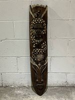 Full view of the tall narrow wooden mask showing the bird of prey at the top, coiled serpent in the middle, armadillo below it and human face at the bottom.