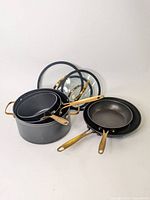Full set of black pots and pans with brass handles, some stacked with glass lids shown.
