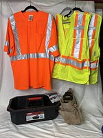 Photo shows the bright orange reflective t-shirt and two yellow reflective vests hanging, a pair of gloves, a Dewalt clip-on tool pouch, a tan tool belt and the black Husky tool caddy underneath them.
