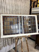 Full view of stained glass window showing wooden white frame and the full design of the leaded glass panes with amber and orange glass