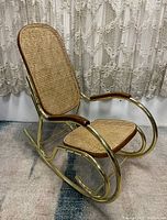 Full side view of the rocking chair showing tubular metal frame, cane seat and back, and wooden armrests