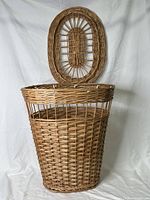 Wicker laundry basket with lid open, showing basket's interior and lid structure.