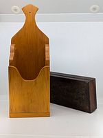 Two wooden home decor items: a light wood wall-mounted holder and a dark carved rectangular box.