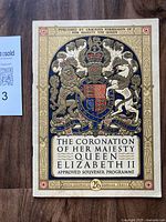Front cover of the Coronation programme showing central Royal Coat of Arms and event title with decorative border in multiple colors.