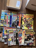 Top-down view of multiple wrestling magazines stacked and fanned out inside a cardboard box featuring Pro Wrestling Illustrated covers with wrestlers and major event headlines.