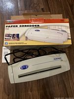 Top and front view of the white Fellowes FS5 paper shredder with visible strip cut slot and power button. Unit has accompanying retail box.