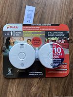 Front view of the Kidde 2-pack smoke alarms in packaging showing product features and images of living areas.