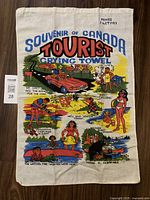 Full view of souvenir tea towel depicting colorful cartoon tourist scenes and text referencing Moose Factory, Canada.