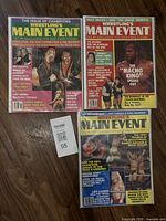 Three Wrestling's Main Event magazines laid flat. Covers show wrestlers including Macho King and Rowdy Roddy Piper with bright, bold text.