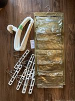 Lot showing white plastic clothes hangers stacked, white plastic clip pants hangers with metal clips grouped, and a beige fabric & clear plastic hanging pocket organizer with multiple pockets.