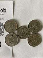 Five UK one shilling coins placed on white paper showing reverse sides with crowned lion design and dates 1948 and 1950.