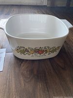 Image of one Corningware La Marjolaine casserole dish showing side floral and fruit pattern with handle and no lid on wooden surface.