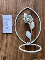 Full view of the white metal wall plant hanger showing twisted oval frame, rose flower, leaves and circular plant holder