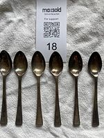 Set of six silver-plated teaspoons laid out on white cloth, tarnished condition.