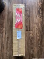 Photo of a cardboard box containing a roll of wallpaper with colorful retro floral pin design adhered to the box for display.