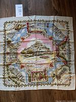 Full view of the 25-inch square souvenir scarf showing a central pink panel surrounded by detailed illustrations of Edinburgh landmarks and floral borders.