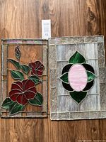 Two stained glass panels side by side on wooden surface, one with red flowers and one with a pink oval pattern