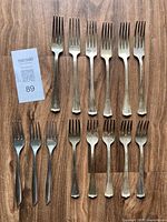 14 forks laid out on wooden surface, arranged to show both dinner and dessert forks.