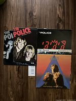 Five vinyl record album covers from The Police arranged overlapping on a floor showing Outlandos d'Amour, Reggatta de Blanc, Synchronicity, and Zenyatta Mondatta.