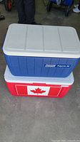Two Coleman coolers stacked: blue Polylite 34 on top, red cooler with Canadian flag decal on bottom.