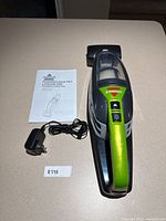 Top view of the black and green Bissell PowerClean Pet Lithium Ion cordless hand vacuum along with its instruction manual and charging adapter on a beige table.