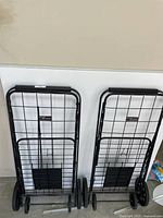 Two folded Easy-O-Wheels large folding utility carts side by side against a white wall.