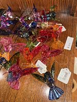 Top-down view showing 11 colorful glass hummingbird figurines on a wooden surface, each with hanging wire attached.