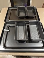 Multiple black non-stick rectangular baking trays and loaf pans stacked on a kitchen counter.