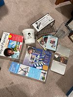 Full lot overview showing all included items: boxed Bob Ross paint set, instructional DVDs, painting bucket, easel box, oil painting kit, painting booklet, and wire basket stand