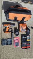 Photo of full set laid out: orange/black Rigid drill, two batteries, charger, handle, three bit kits including a red packaged bolt remover set, and orange/black carrying bag.